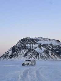 a white van is parked on a snowy road near a mountain